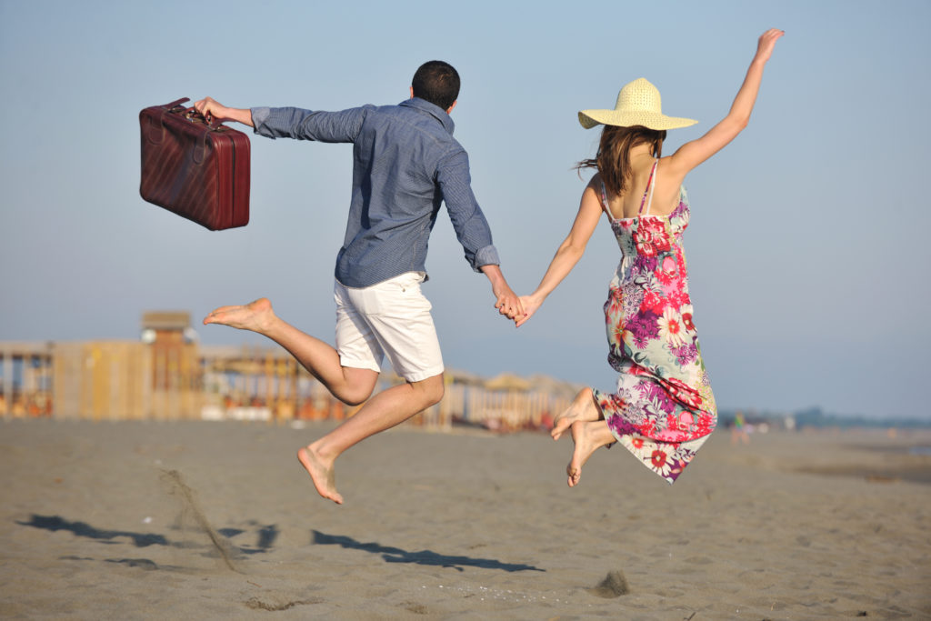 couple on beach with travel bag representing freedom and funy honeymoon concept